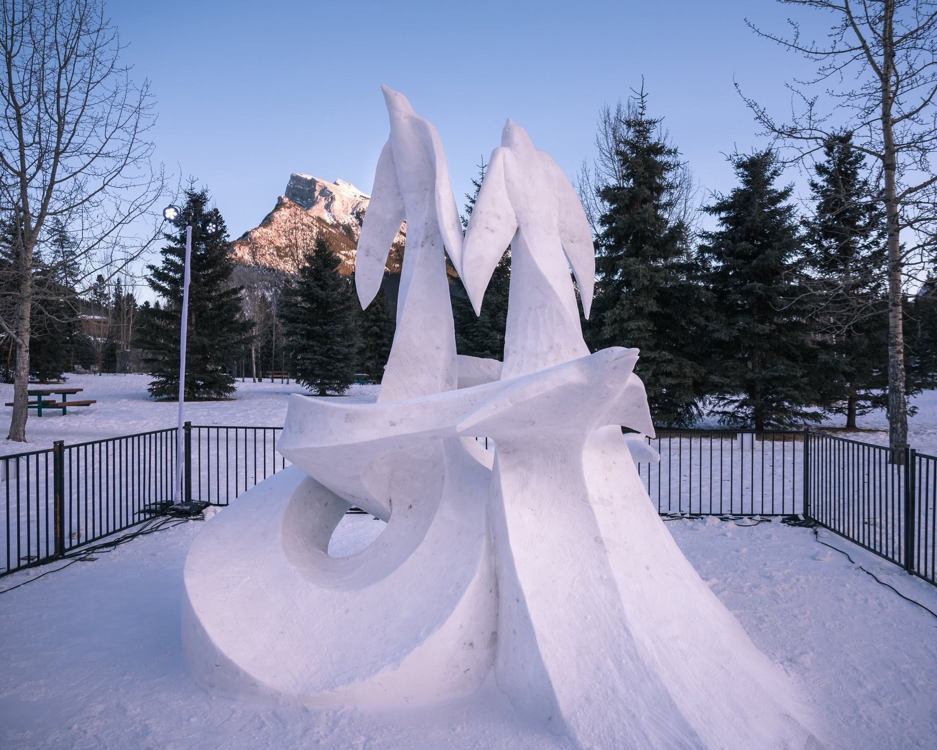 Abstract snow sculpture outdoors with mountain and trees in the background.