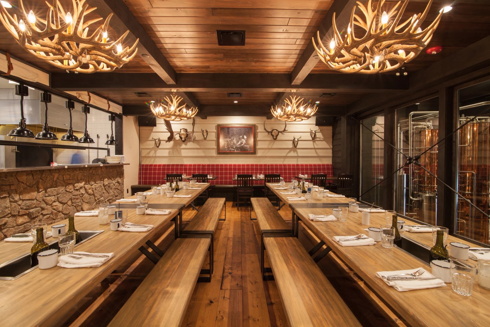 A cozy dining room with wooden tables, antler chandeliers, and a rustic distillery-inspired design.