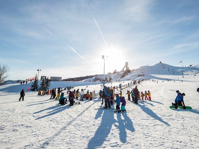 Wide shot of WinSport with kids getting on the bunny hill in the background.