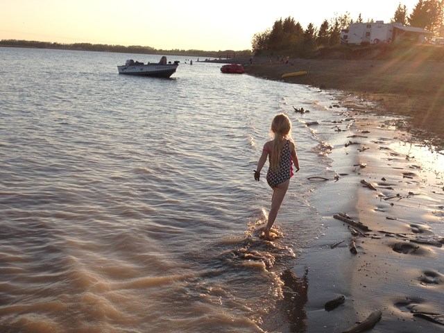 A kids walking through the water close to the shore.