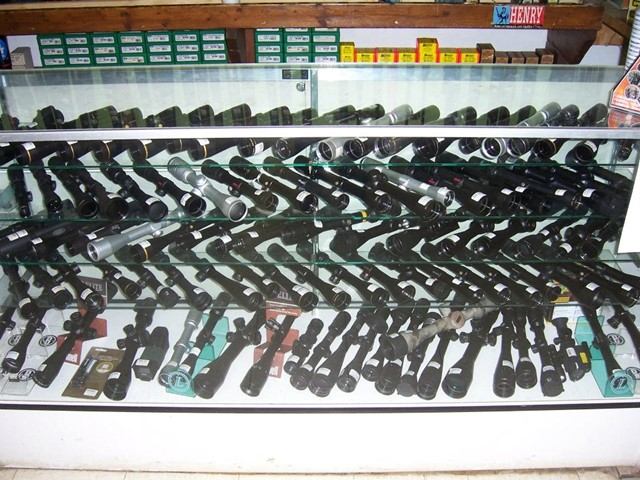 Rifle scopes and optics arranged in a glass display case.
