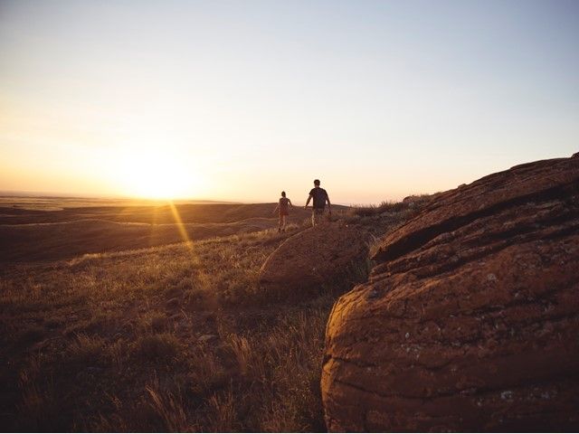 A young couple hiking through large rocks at sunset in Red Rock Coulee Provincial Park.