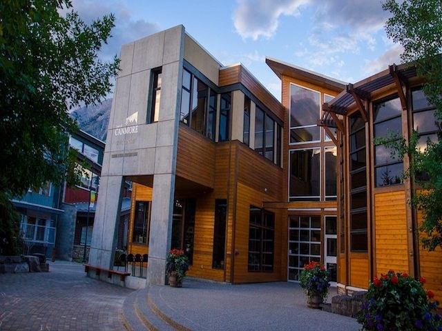 Modern building of wood and concrete, large windows, flower pots, and a scenic blue sky backdrop.