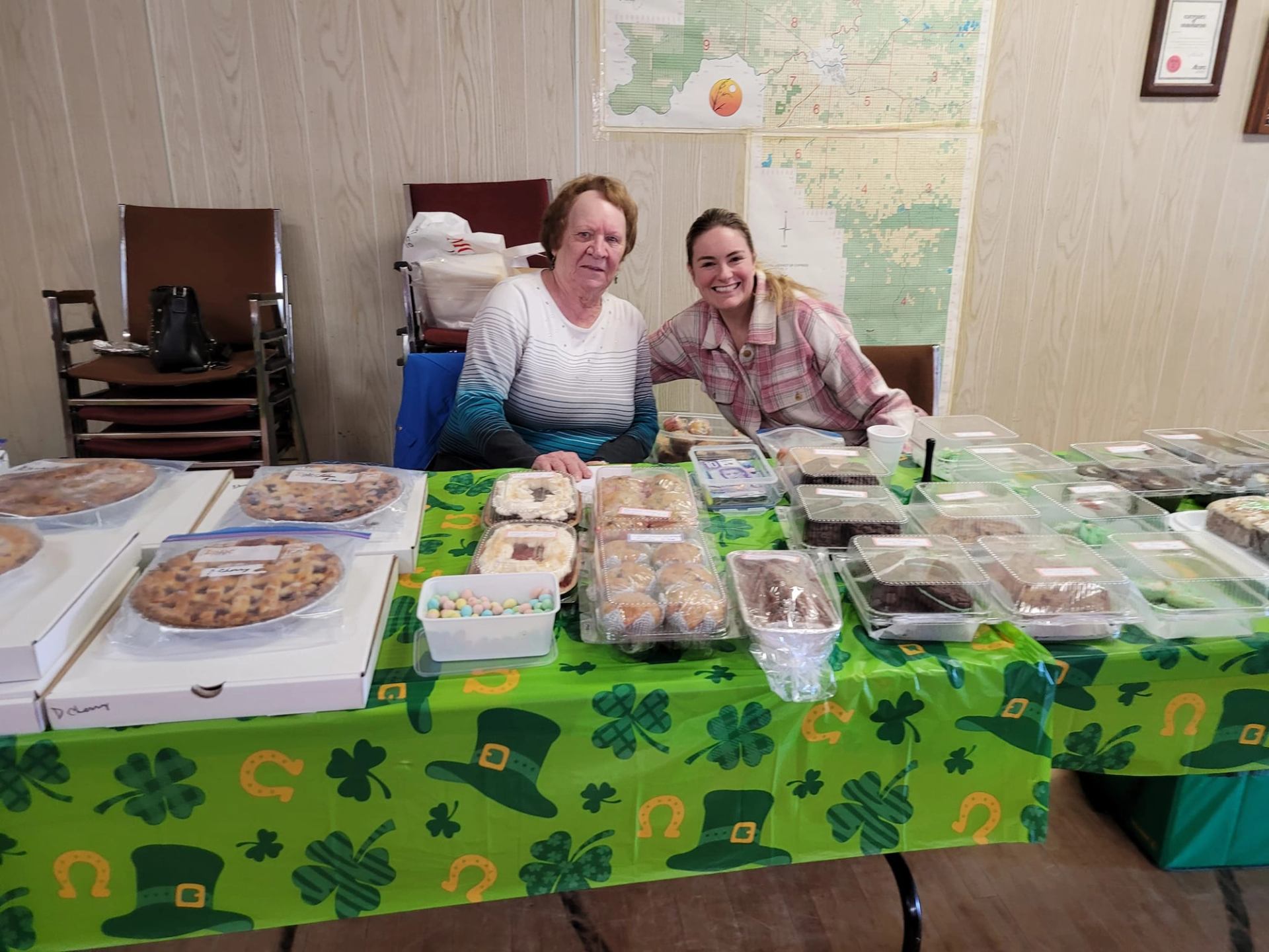 Two women smile behind a St. Patrick's Day-themed table laden with various baked goods.
