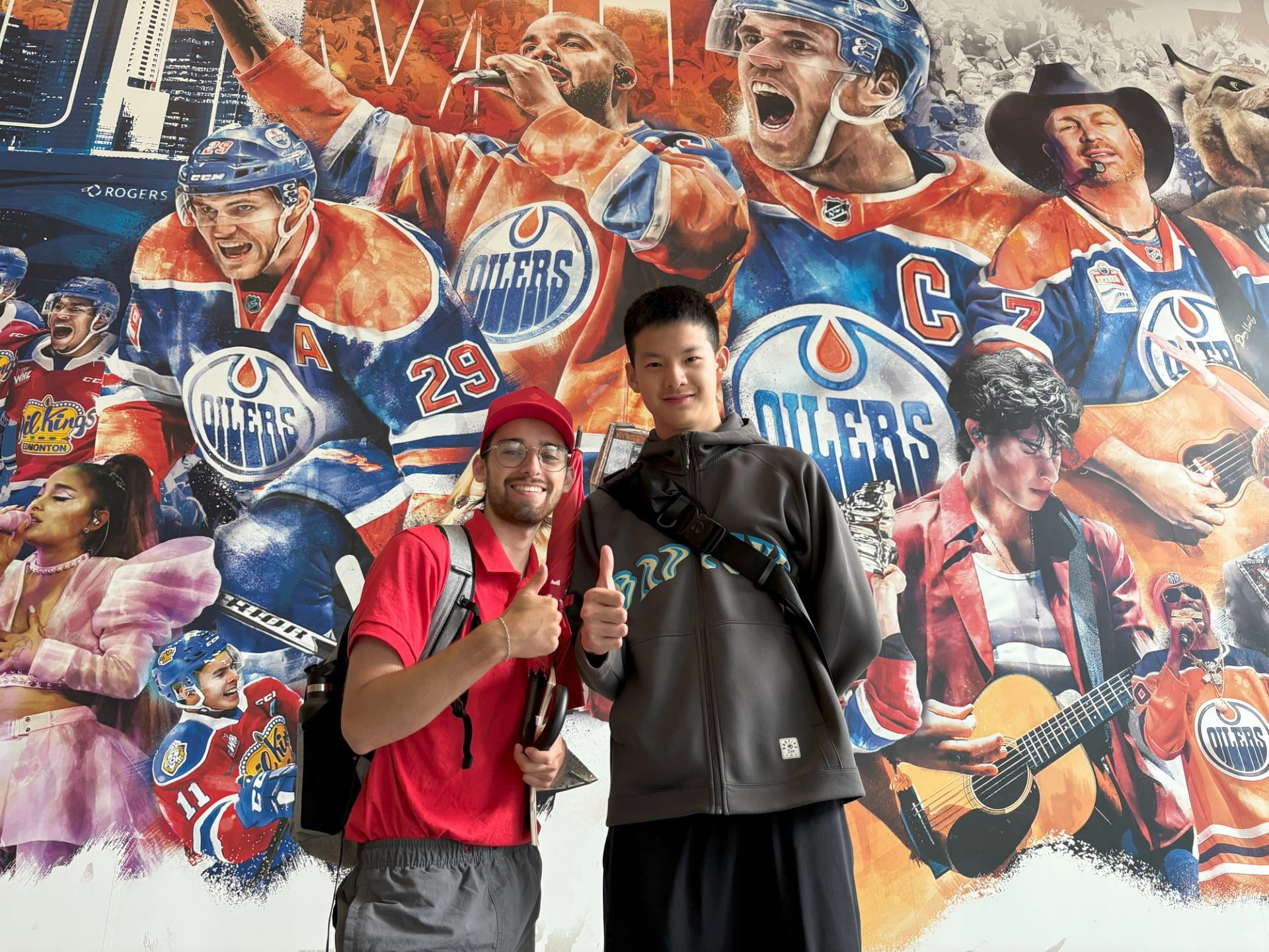 Two people pose in front of a mural featuring Edmonton Oilers and local culture.