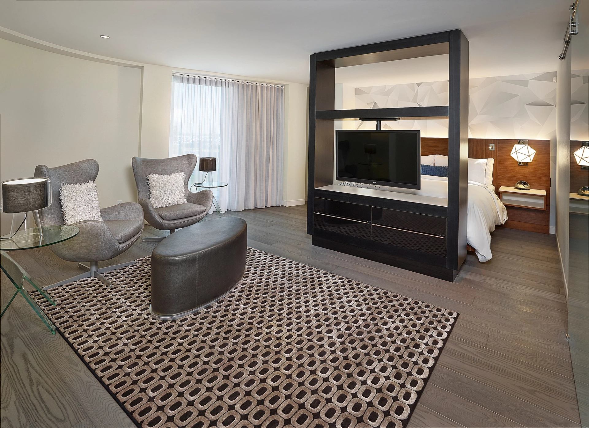 Spacious hotel suite with bed, lounge chairs, and modern partition.