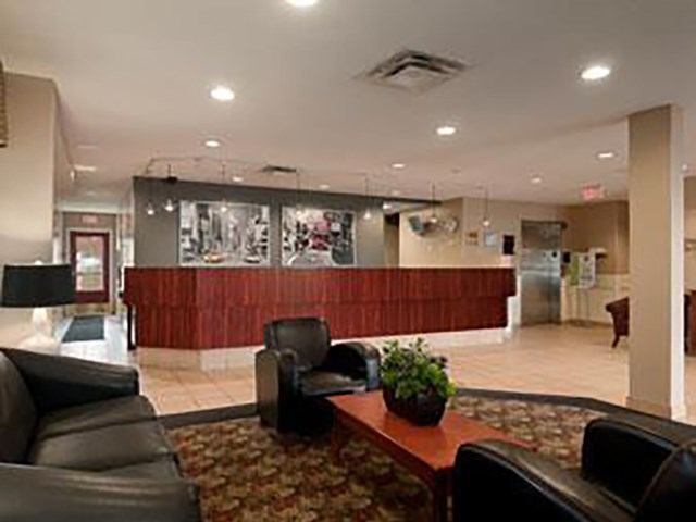 A hotel lobby with a dark wood reception desk and a seating area featuring black leather furniture, a coffee table, and a patterned rug.