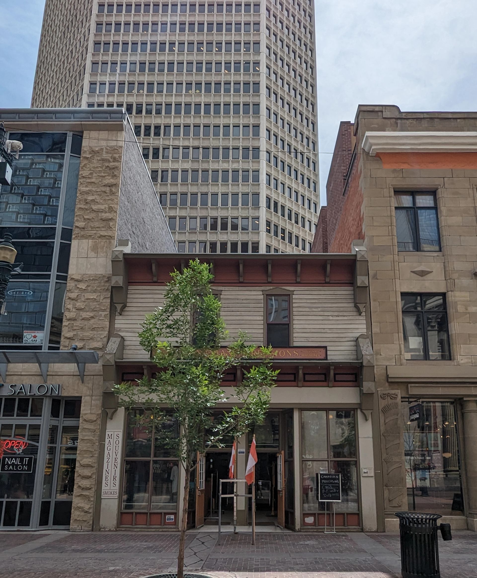Downtown street scene with small shop, flags at entrance, and tall office tower.