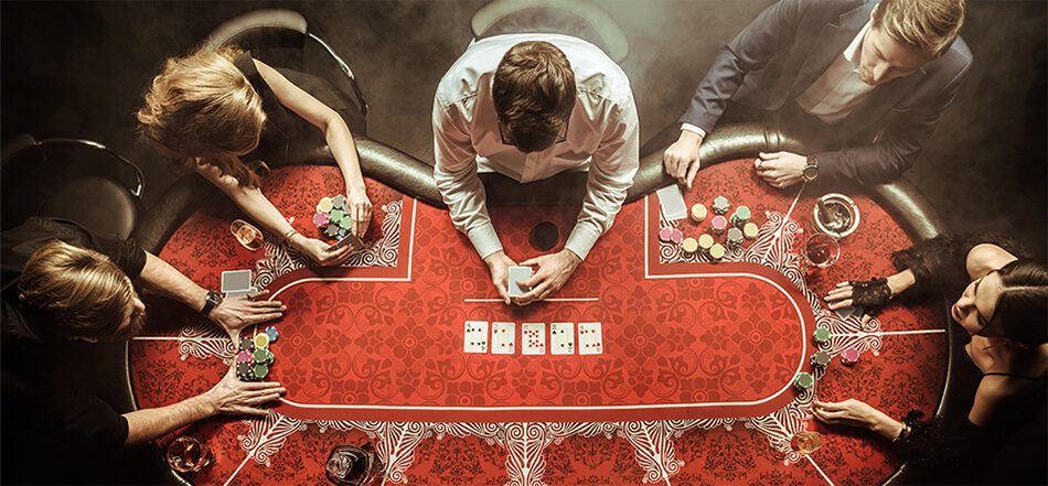 Five players are seated around a poker table featuring playing cards, chips, and a red felt surface.