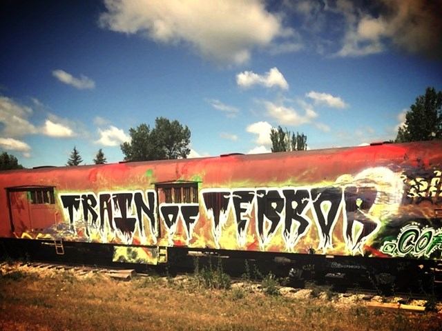Red train car with graffiti-style text reading "Train of Terror" against a sunny sky and trees.