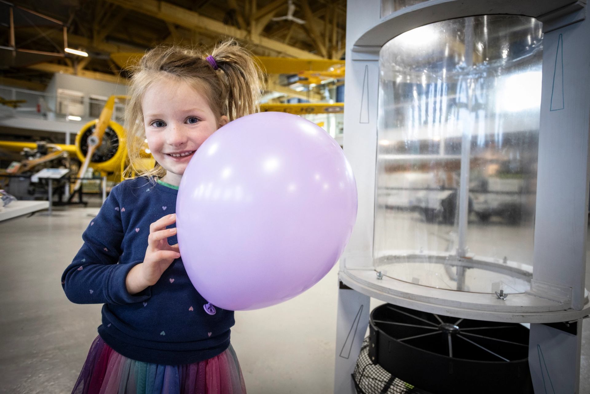 Child with balloon explores aviation exhibit at The Hangar Flight Museum.