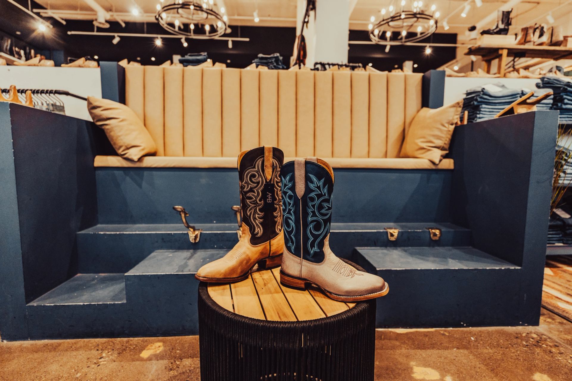 Pair of embroidered cowboy boots on round table in clothing store seating area.