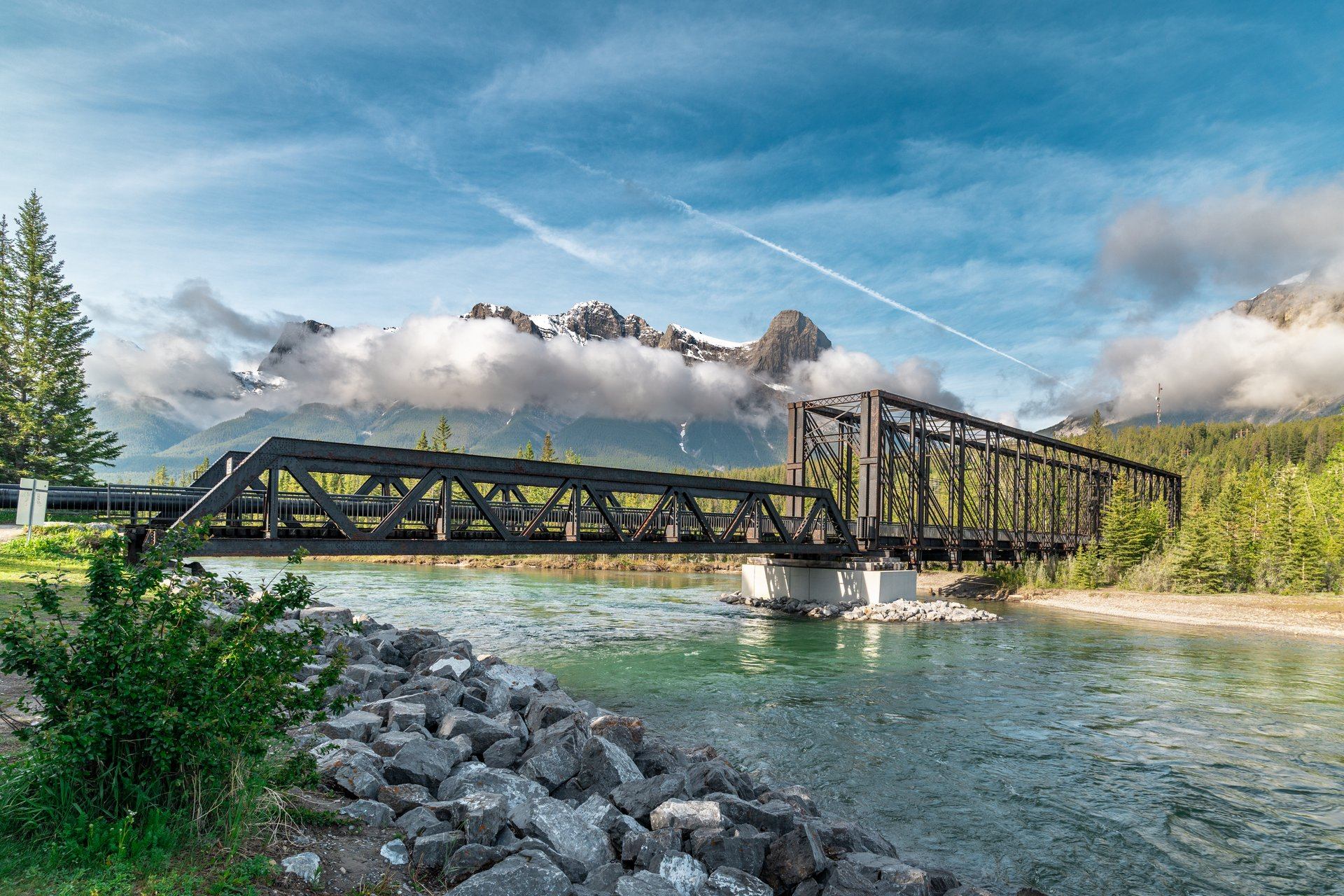 Canmore Engine Bridge in the summer with blue skies, clouds, and mountains in the background.