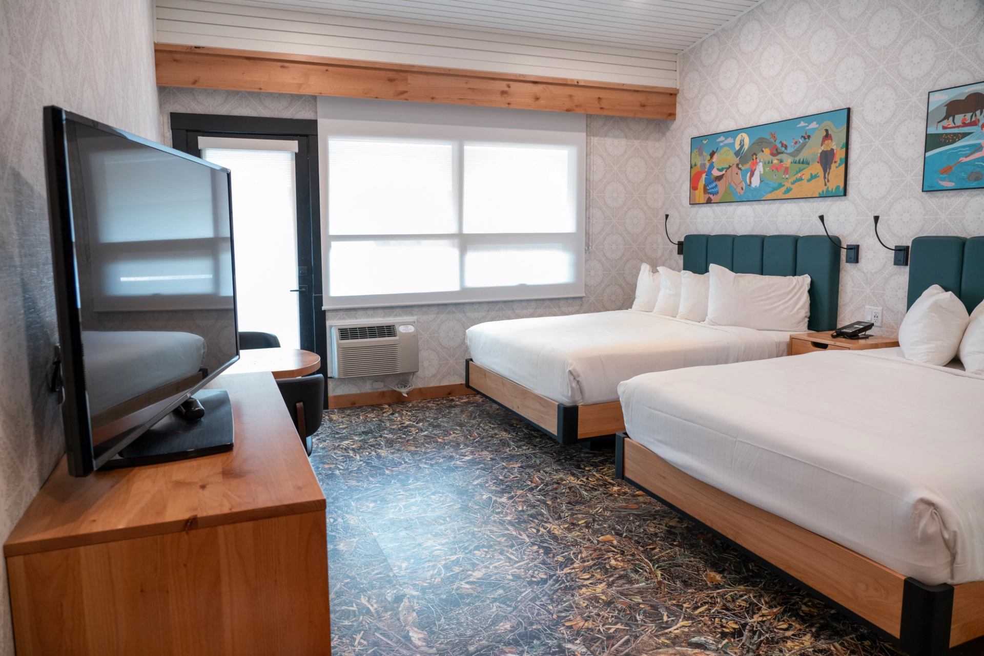Modern motel room with two beds, flat-screen TV, and colorful wall art.