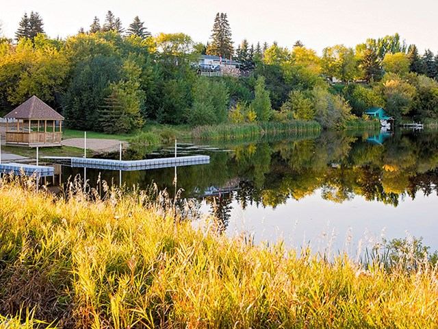 Scenic lake surrounded by trees with a dock and gazebo reflecting in calm water