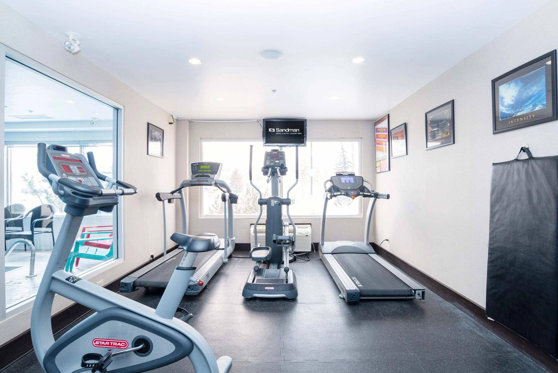 Small fitness room with treadmills, exercise bike, elliptical machine and Sandman TV screen.