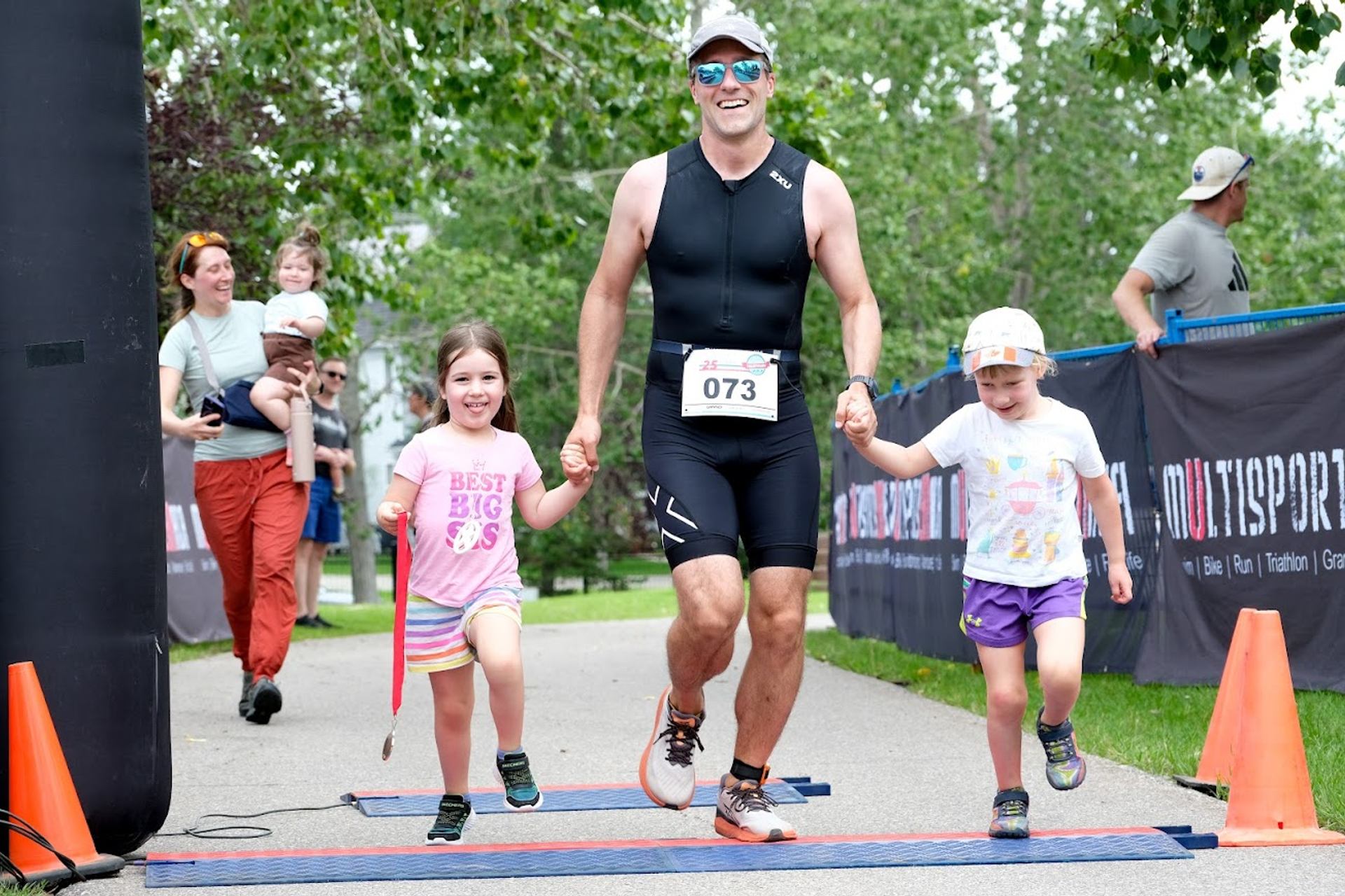 Athlete finishing Lake Chaparral Triathlon holding hands with two children at the finish line.