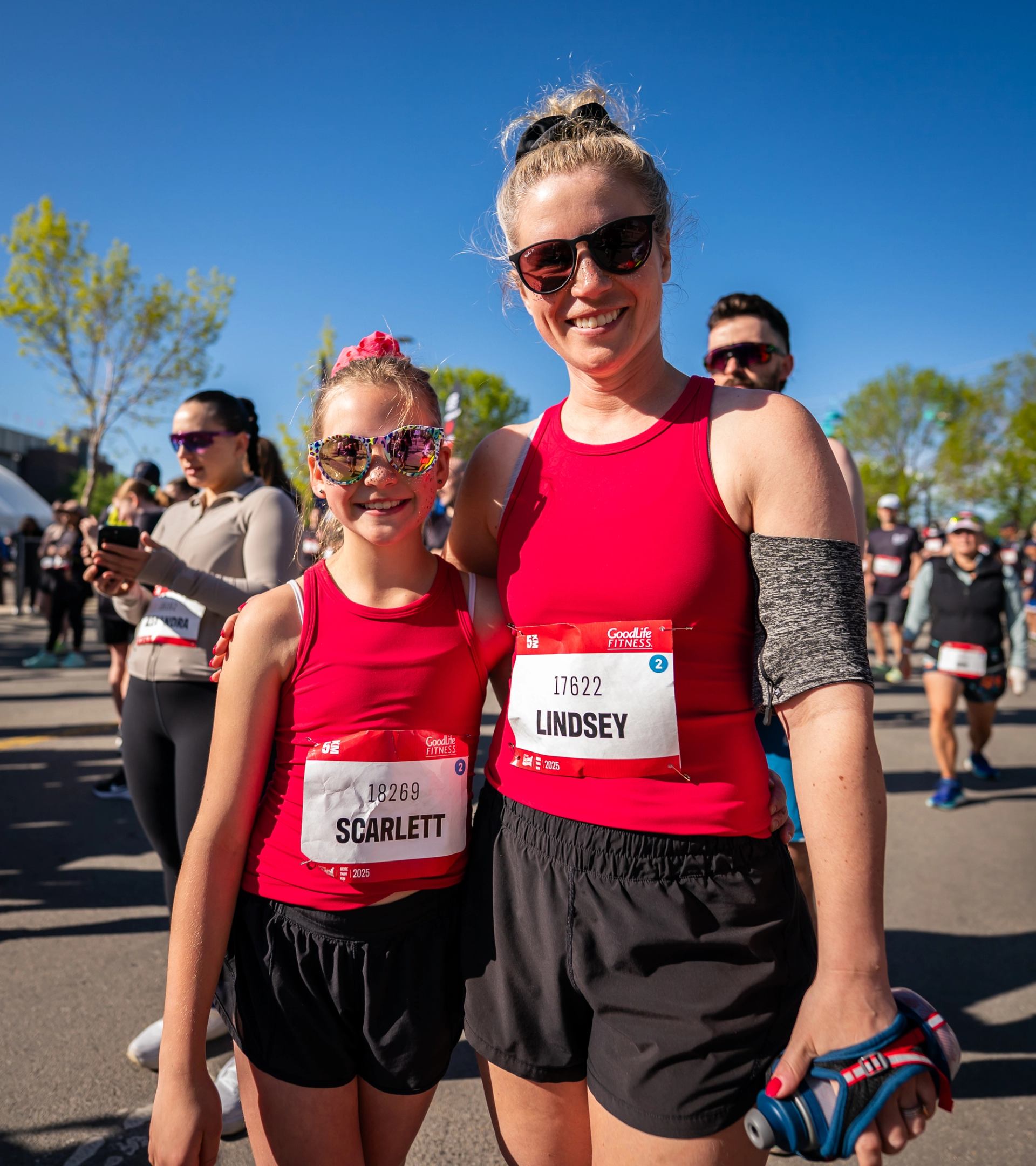Runners in red tops with bibs Scarlett and Lindsey pose amid marathon crowd.