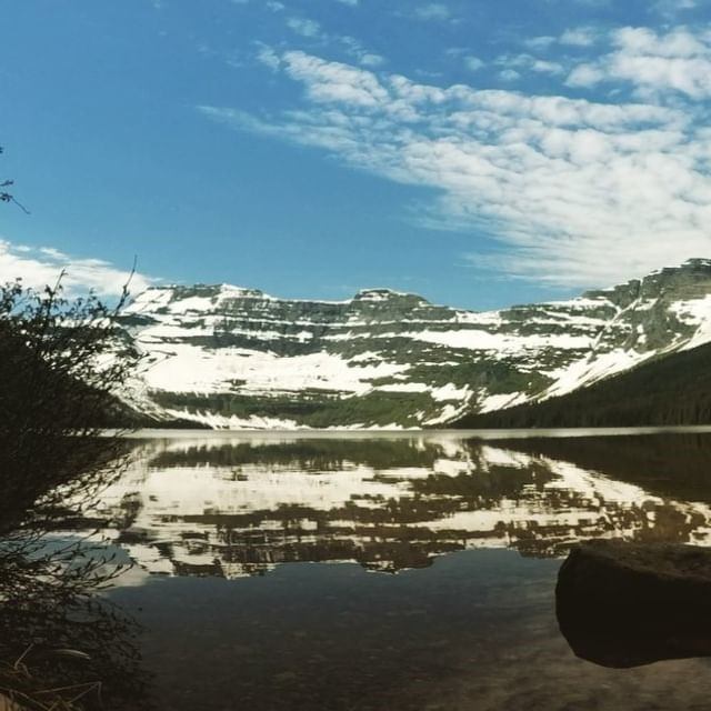 Calm lake reflecting snow-capped mountains and partly cloudy sky.