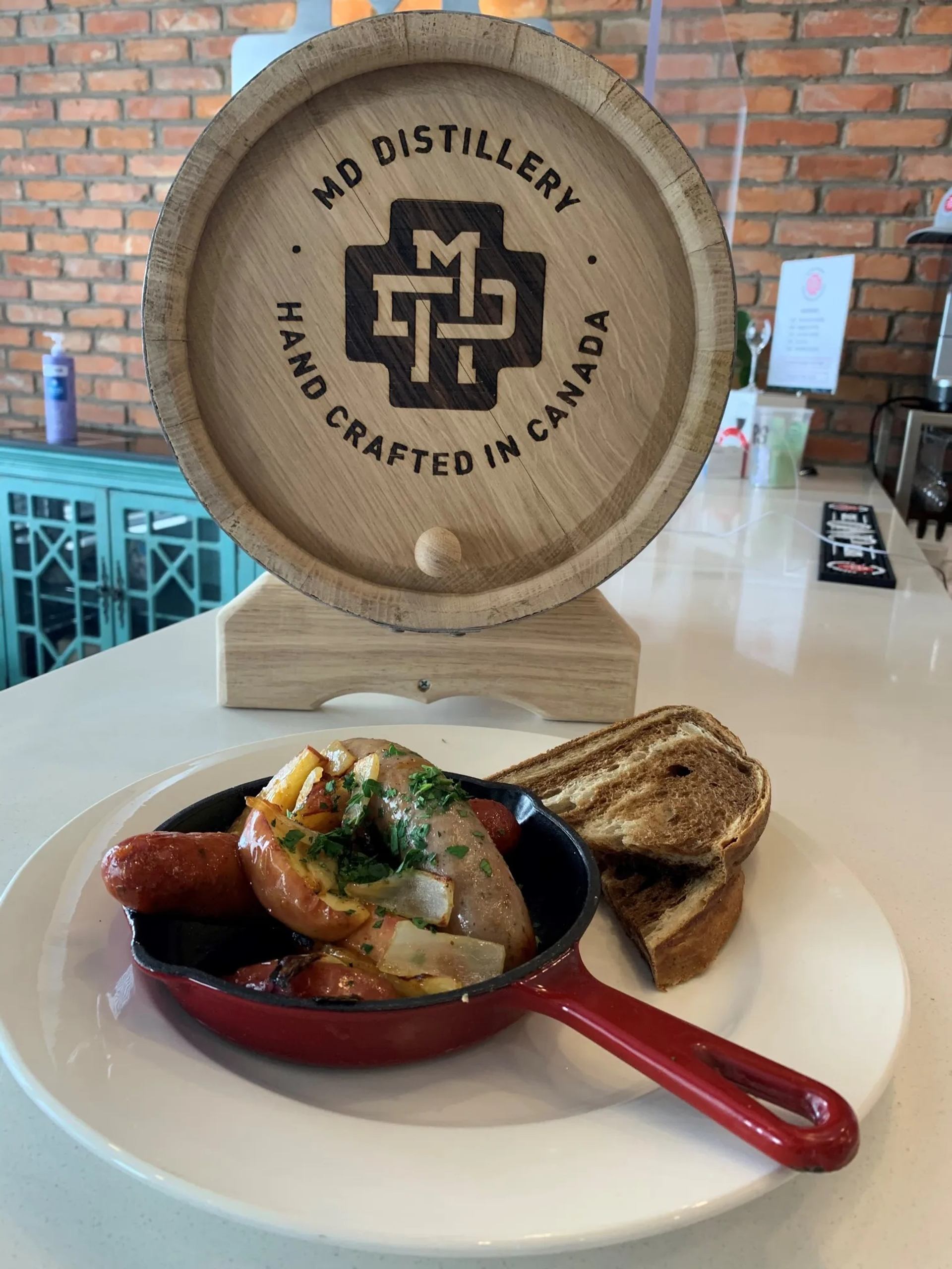 Skillet of sausages with onions and bread in front of MD Distillery barrel.