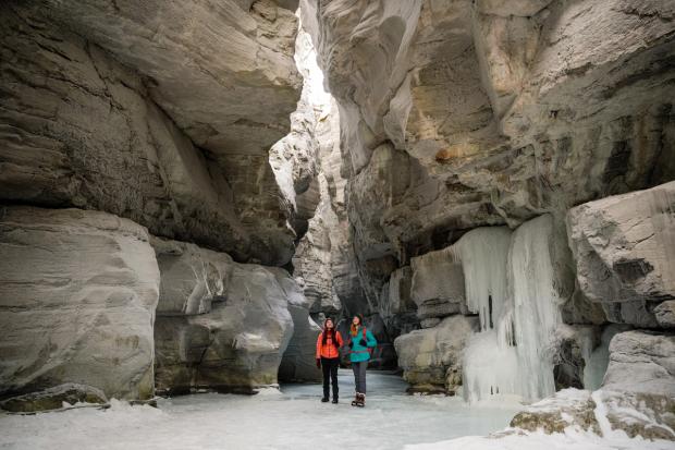 Two friend stand in the middle of the canyon taking in the views while ice walking and winter hiking Maligne Canyon Ice Walk in Jasper National Park.