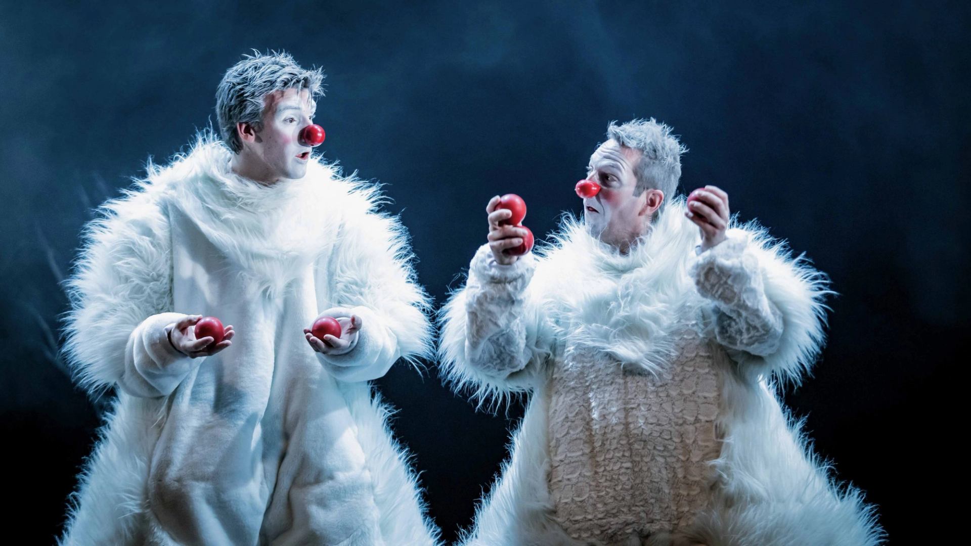 Two performers in furry white costumes juggle red balls with red clown noses.