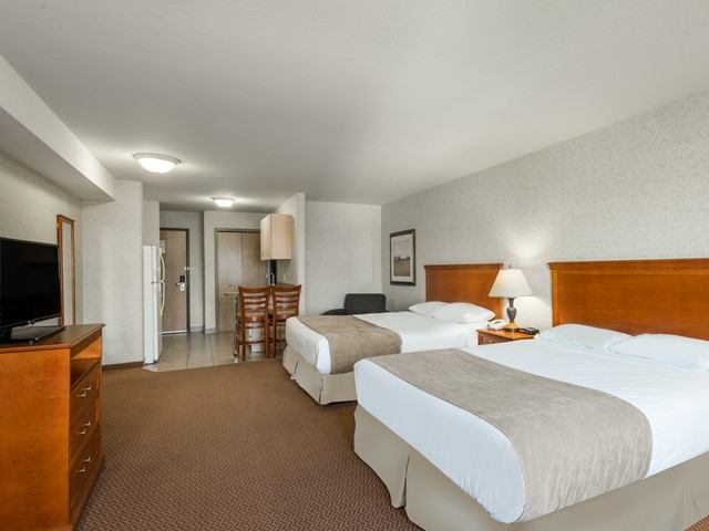 Hotel room with two beds, TV, small dining table, fridge and entryway.