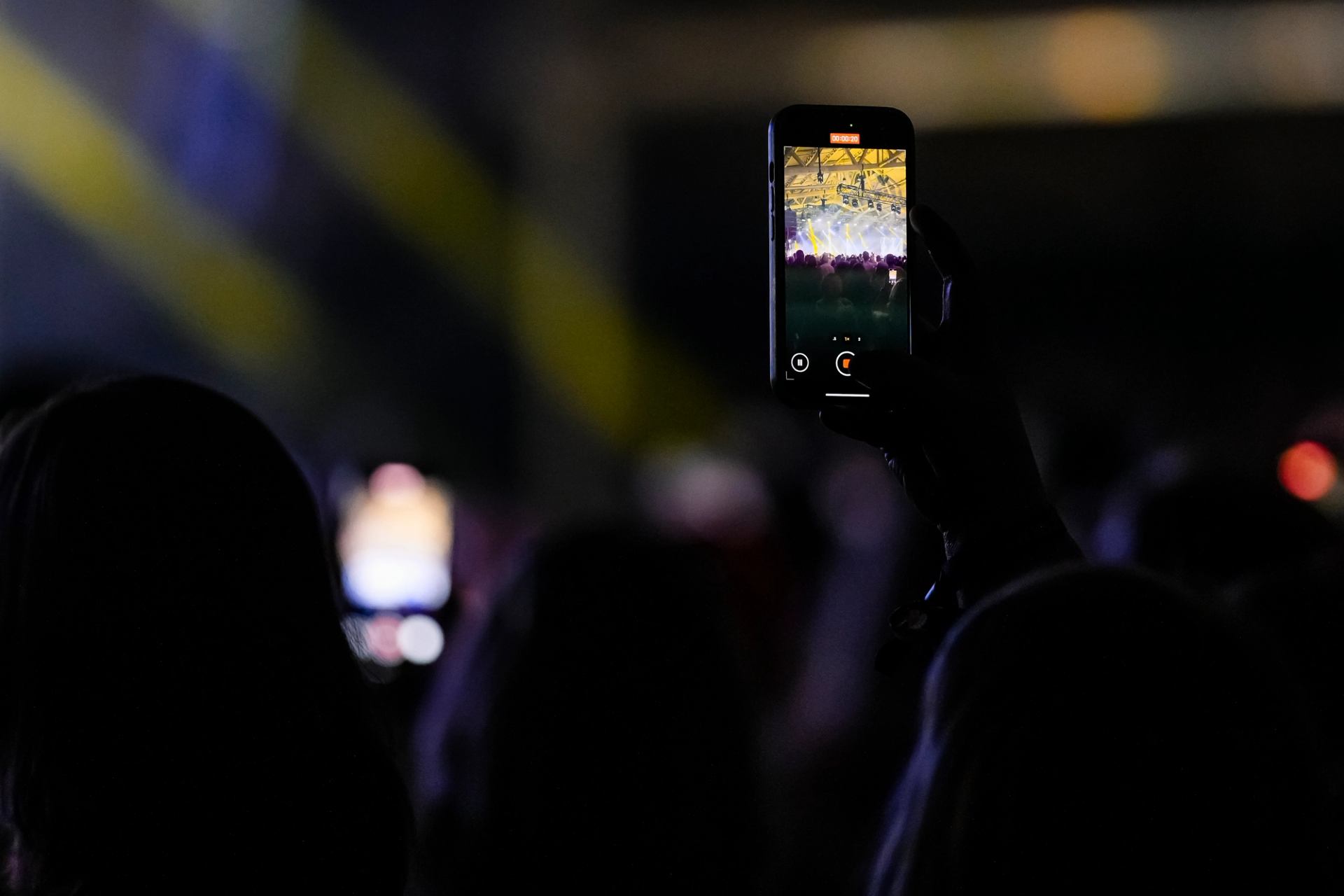A phone held up recording a concert with bright stage lights in the background.