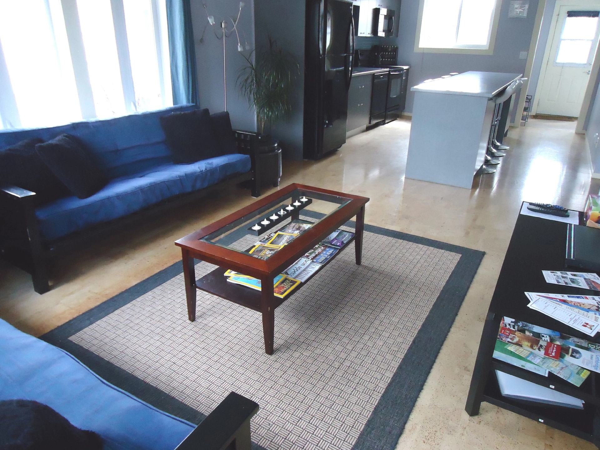 Open-plan living room and kitchen with blue sofas, coffee table and island stools.