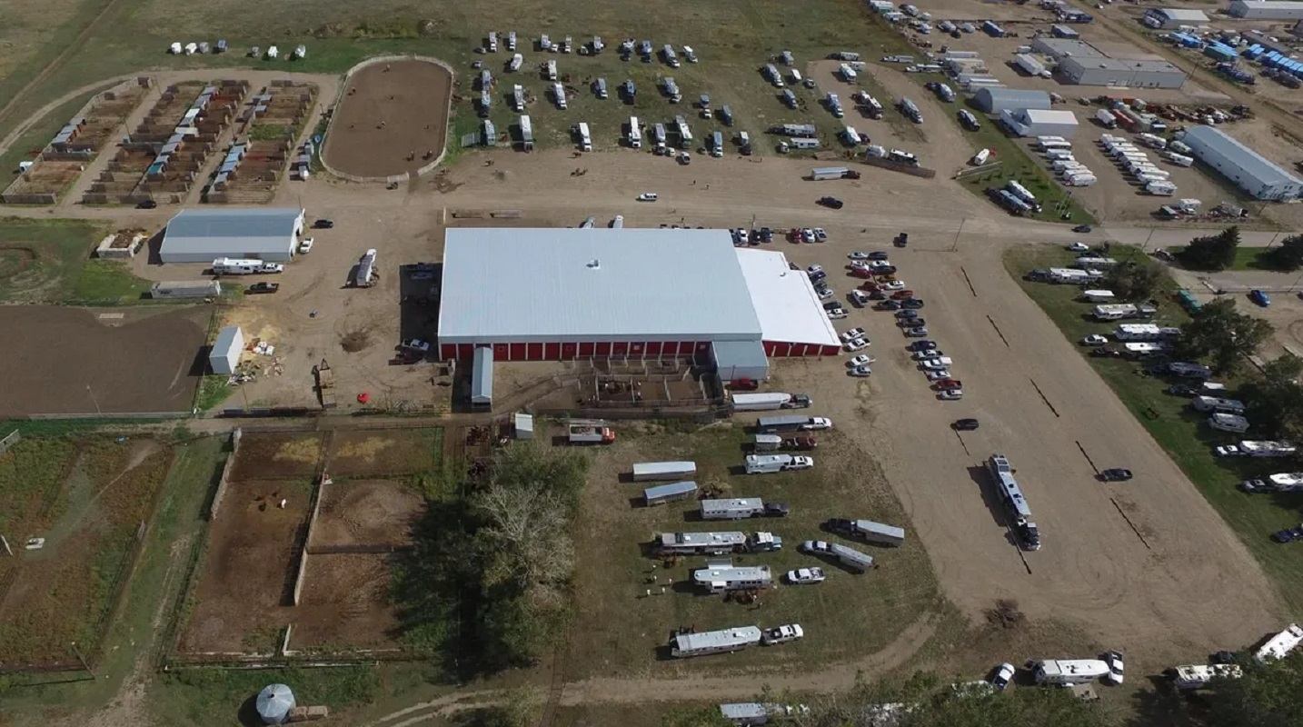 Aerial view of rodeo grounds with barns, arenas, vehicles, and trailers spread across the area.