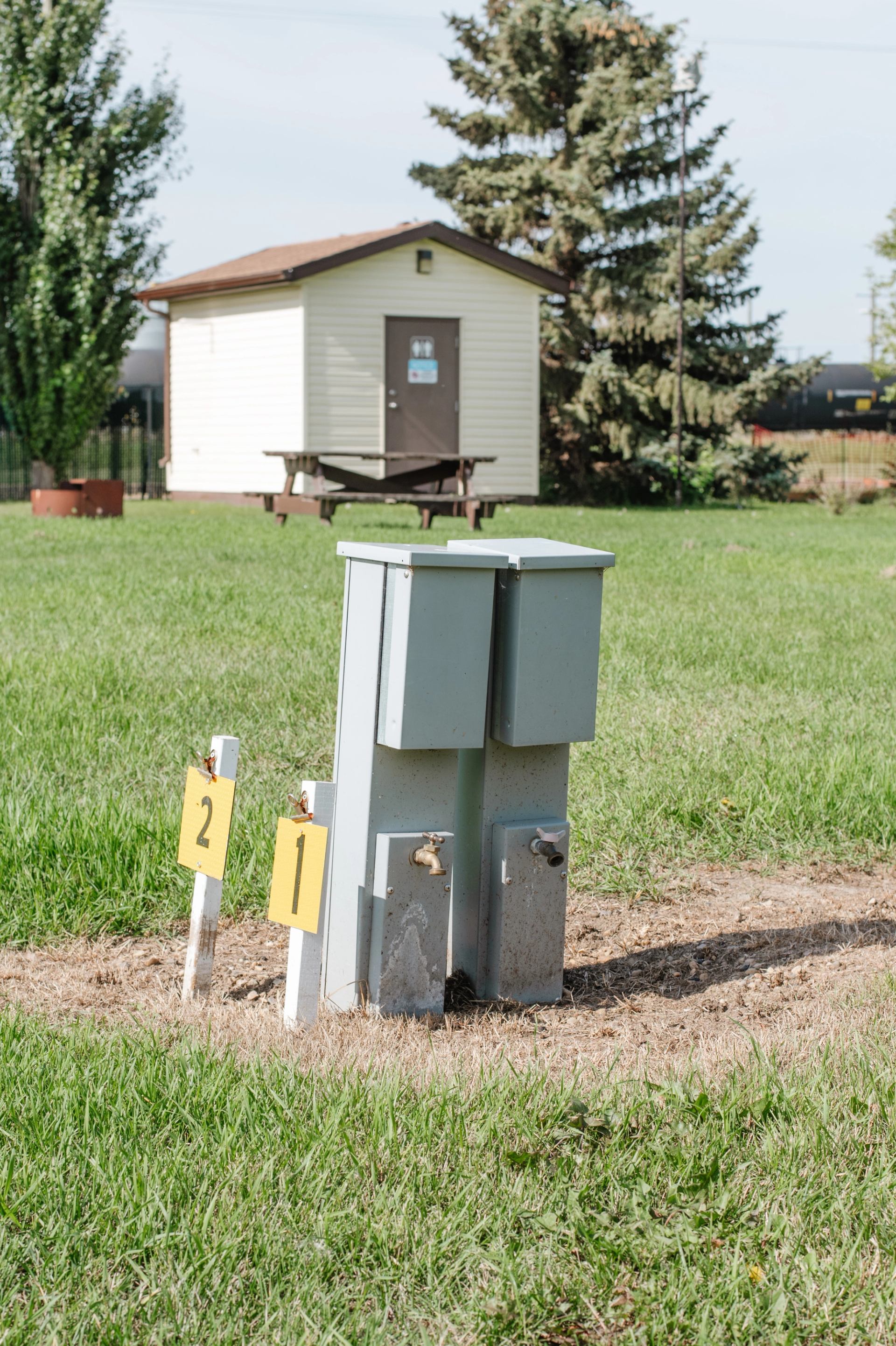 Utility hookups with numbered markers in grassy area, small building and trees behind.