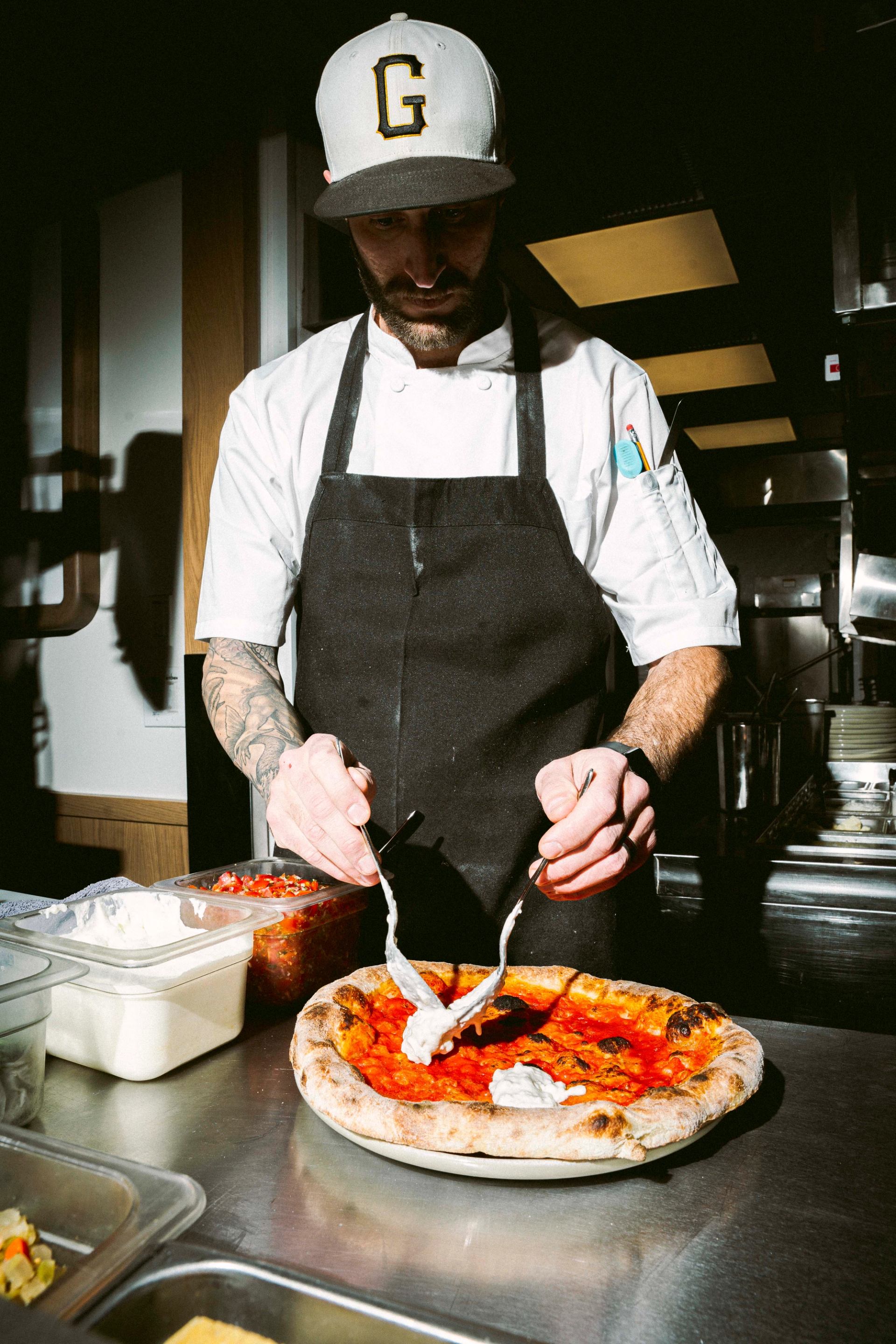 A chef preparing a fresh pizza with tomato sauce and toppings in a kitchen.