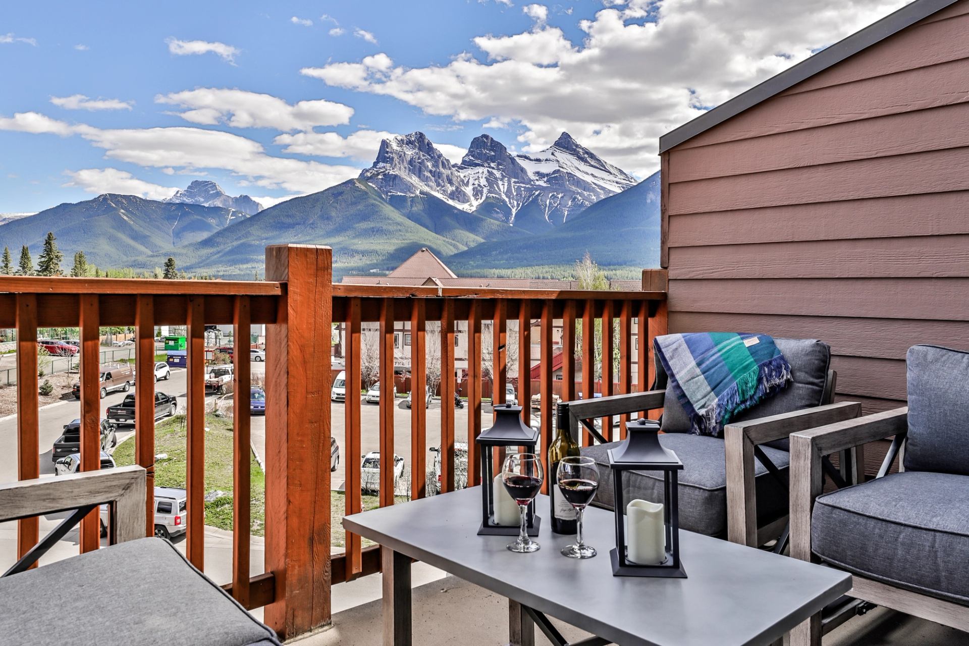 Balcony seating overlooks snow-capped mountains, with wine glasses and lanterns on a table.