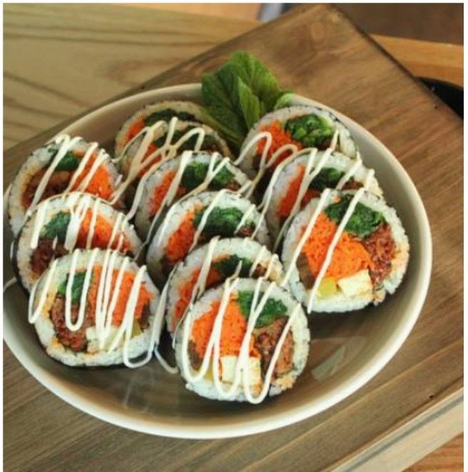 Bowl of sliced rice rolls drizzled with white sauce on wooden table.
