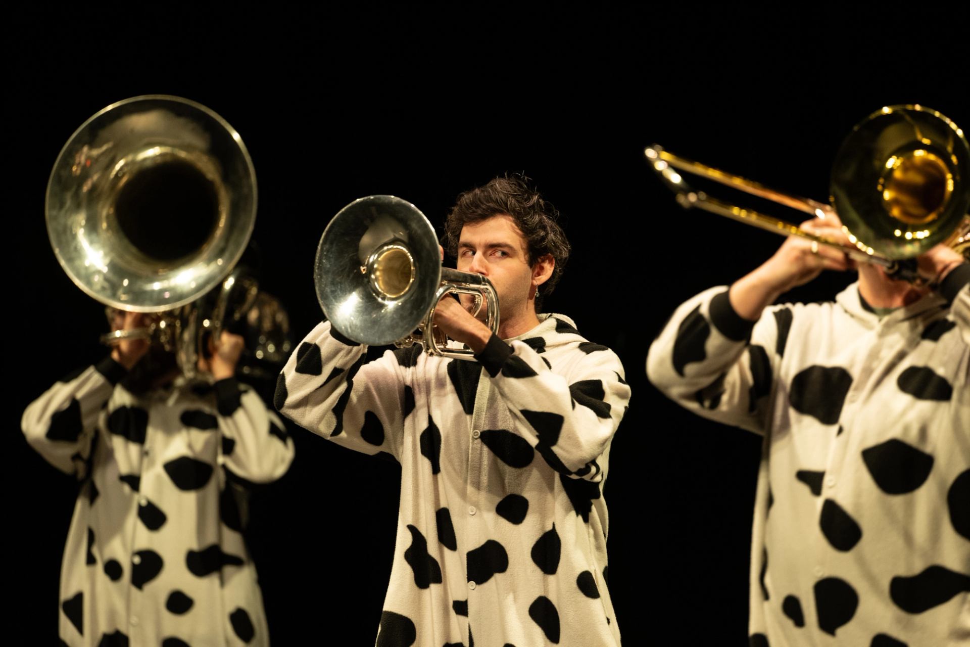 Performers dressed as cows play brass instruments on stage.