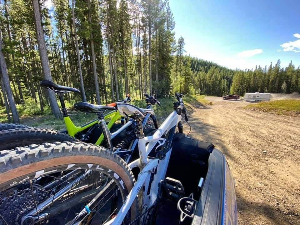 Bicycles mounted on a vehicle at a forest trailhead under a clear blue sky.