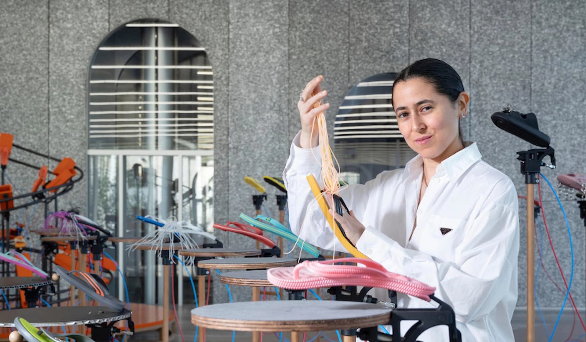 Person in white shirt adjusts colourful plastic tubes on circular tables in studio.