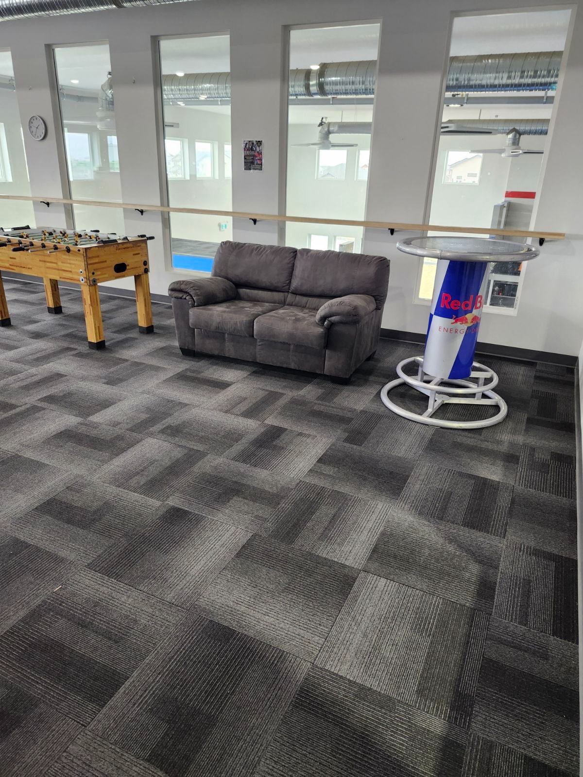 Indoor sports lounge with grey sofa, foosball table, and foosball red drink cooler.
