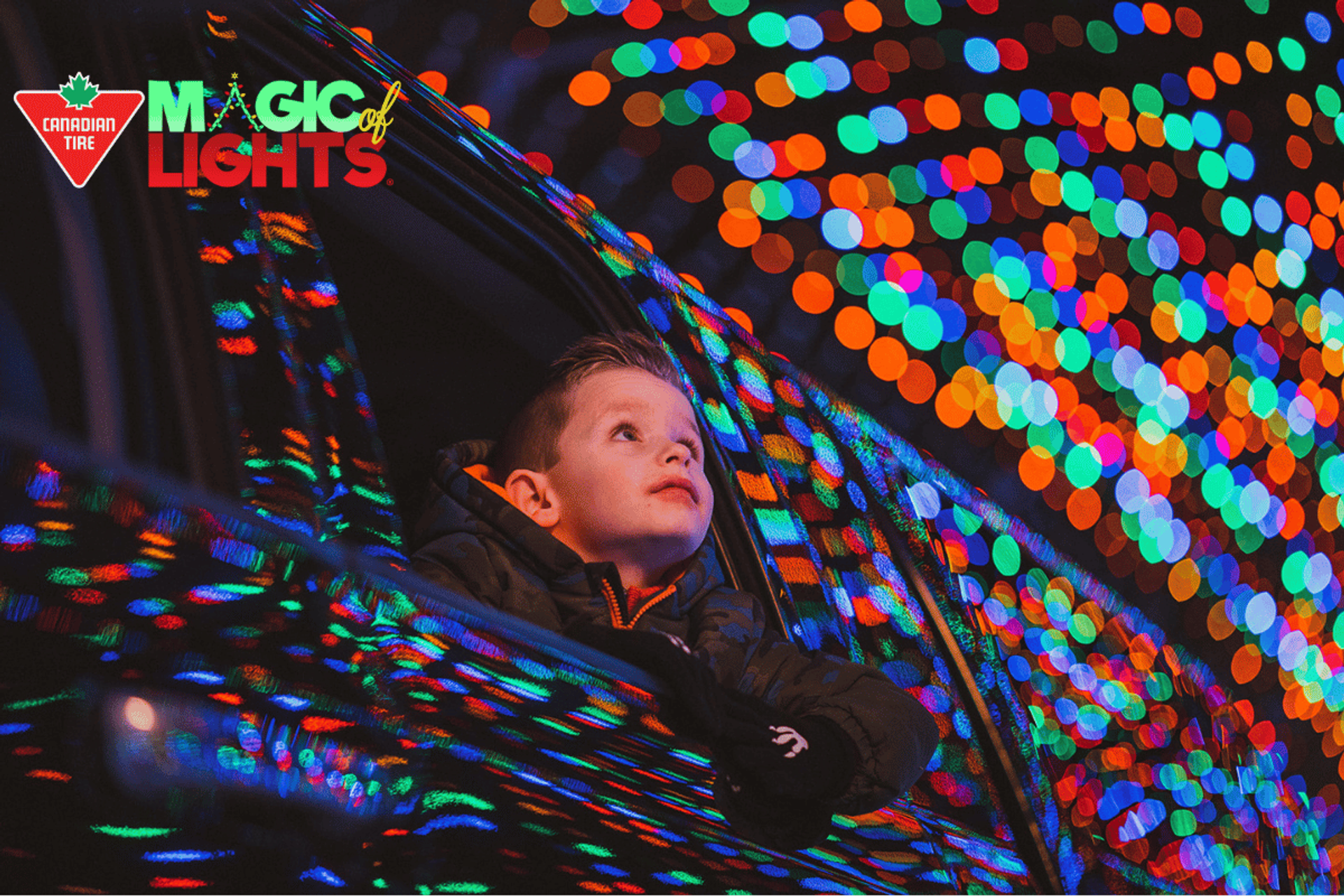 Person leaning out of a car window surrounded by vibrant holiday lights at Magic of Lights.