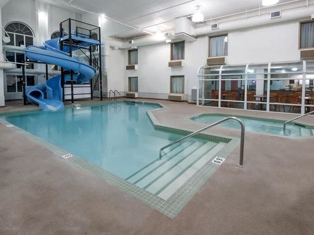 Indoor pool area with blue waterslide, hot tub, and seating behind glass.