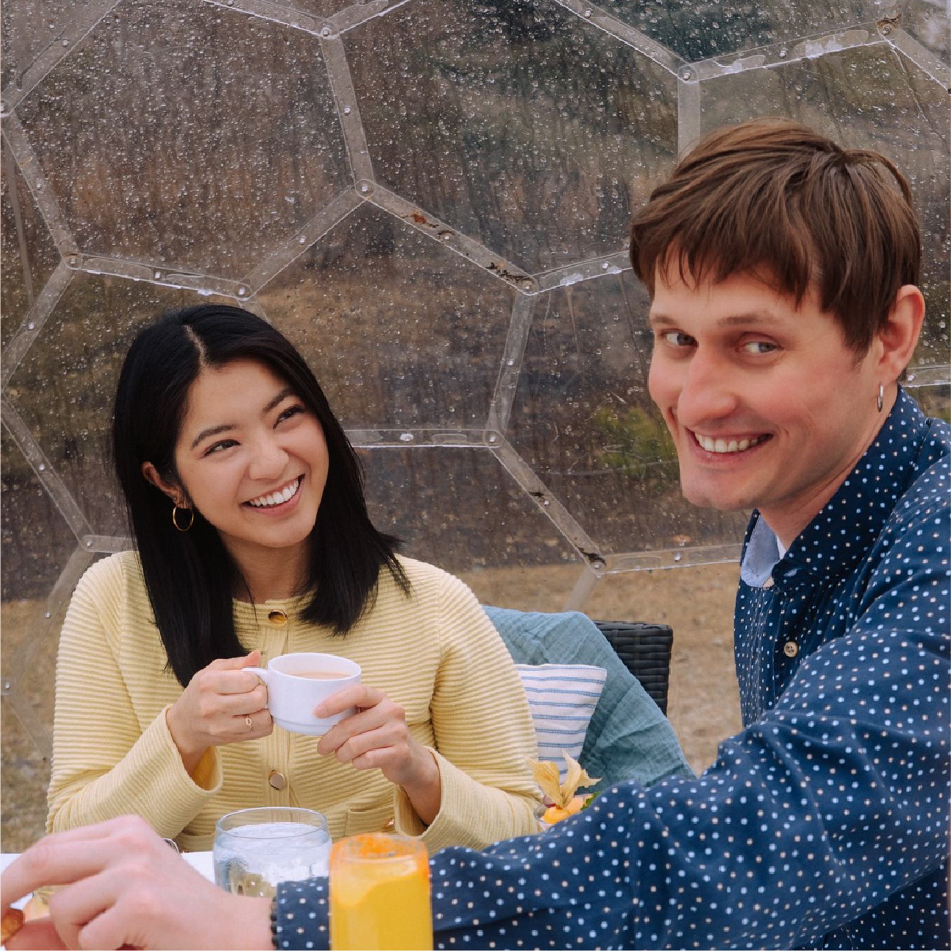 Two people smile over drinks inside a clear geodesic dome.