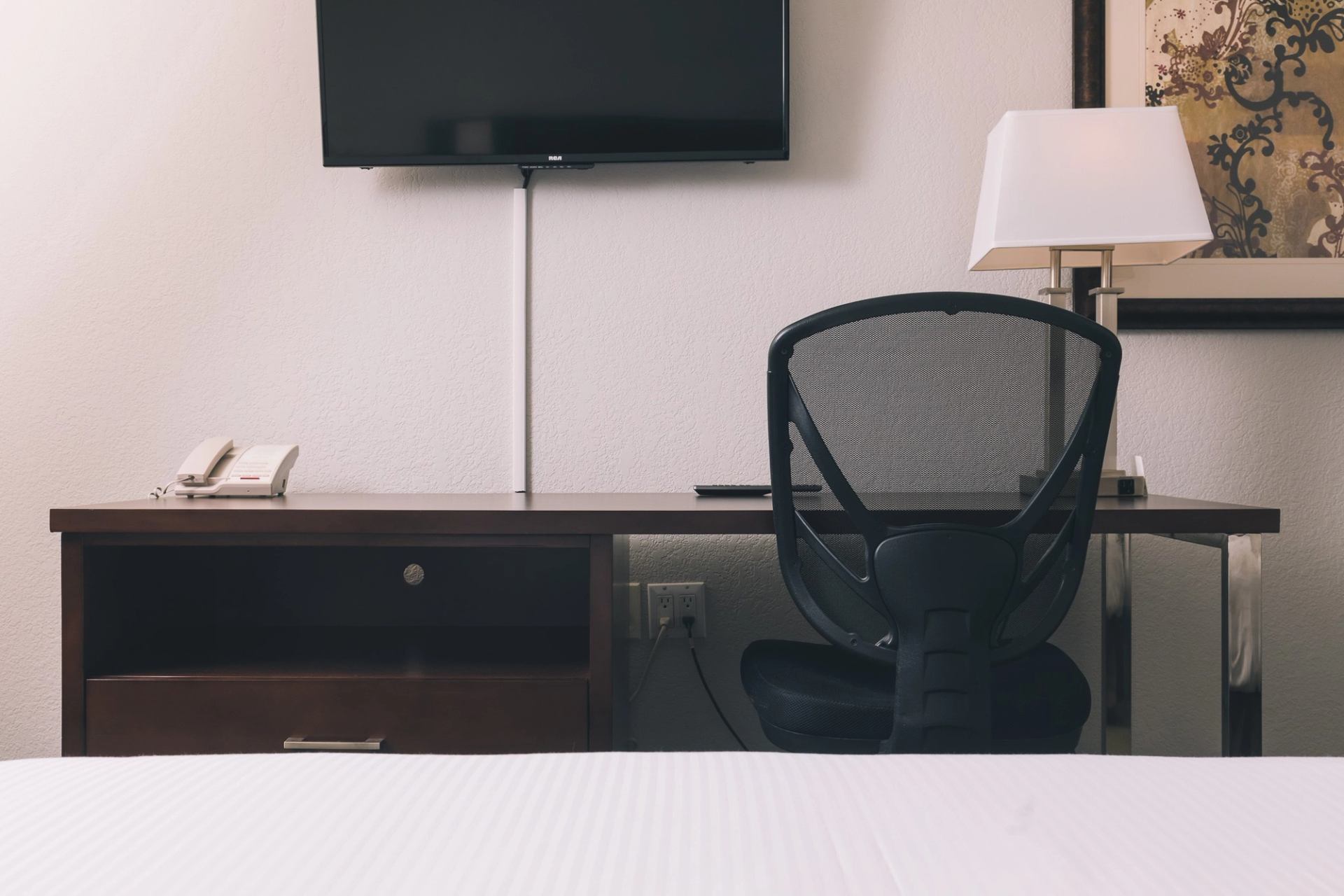 Hotel room desk with chair, lamp, phone and wall-mounted TV.