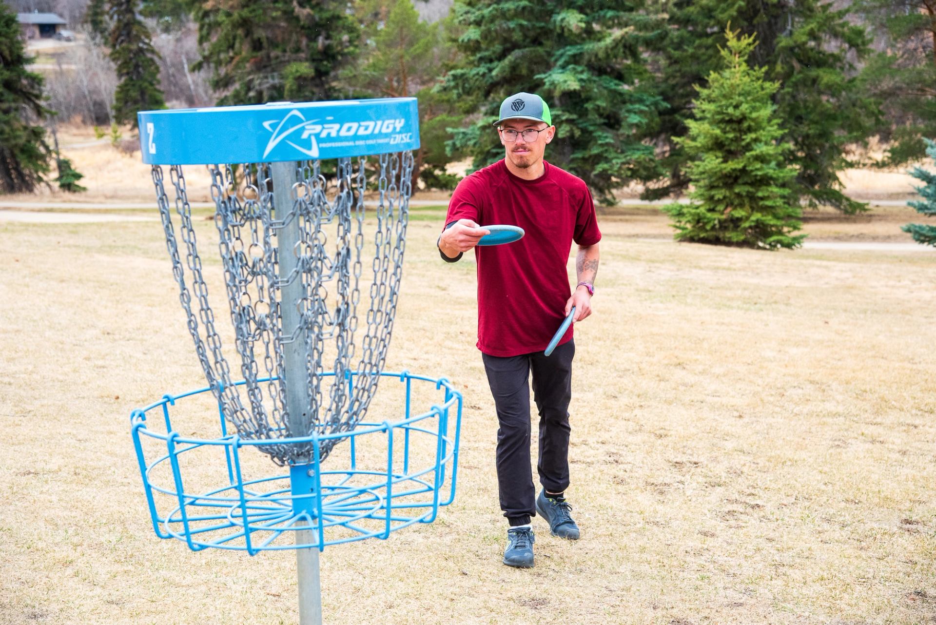 A young adult putting in a disc on hole 2 of the Camrose Disc Golf Course.