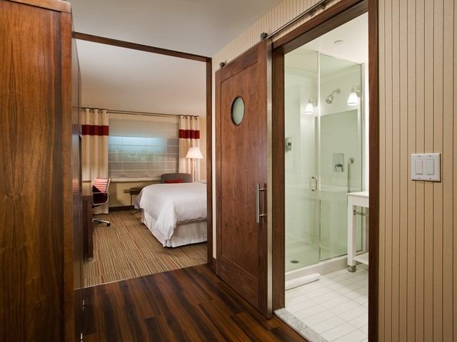 Hotel room with sliding bathroom door, white linens, and red-accented curtains.