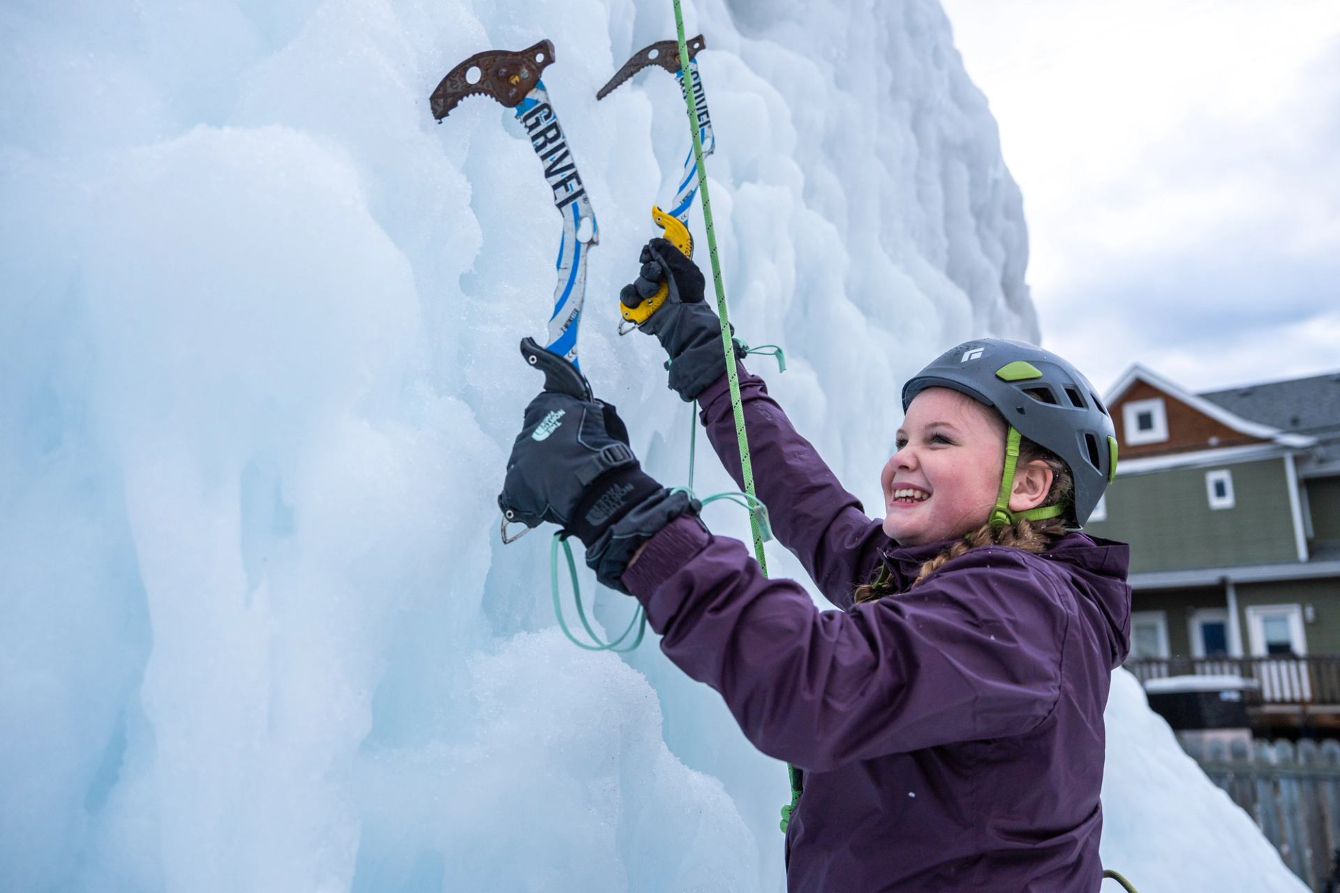 Ice climber scaling frozen wall with axes and ropes near cabins in Jasper.