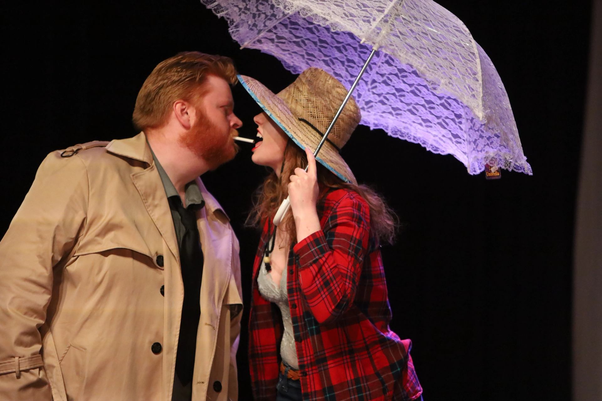 Two performers on stage, one holding a lace parasol and wearing a plaid jacket and straw hat.