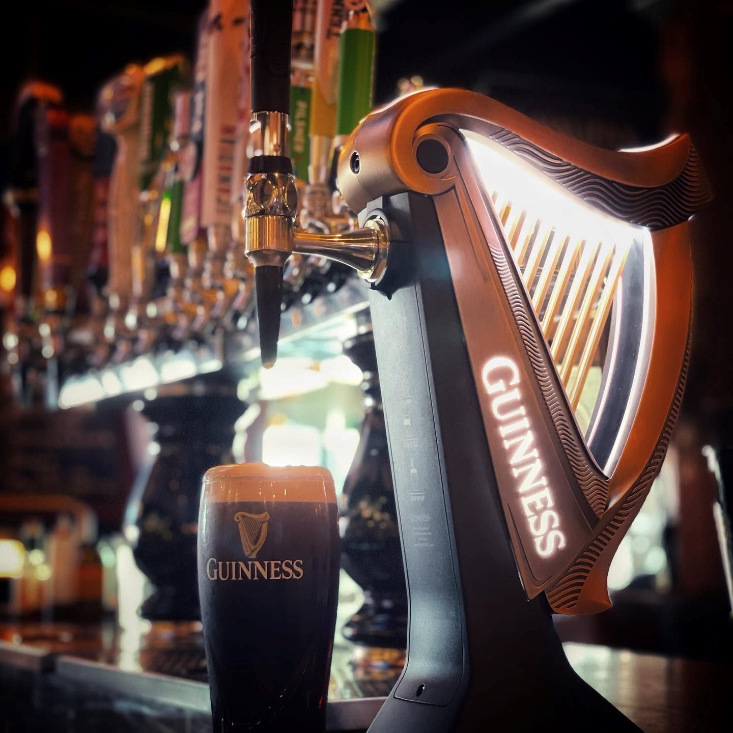 Guinness tap handle with “GUINNESS” glass in a pub bar background.