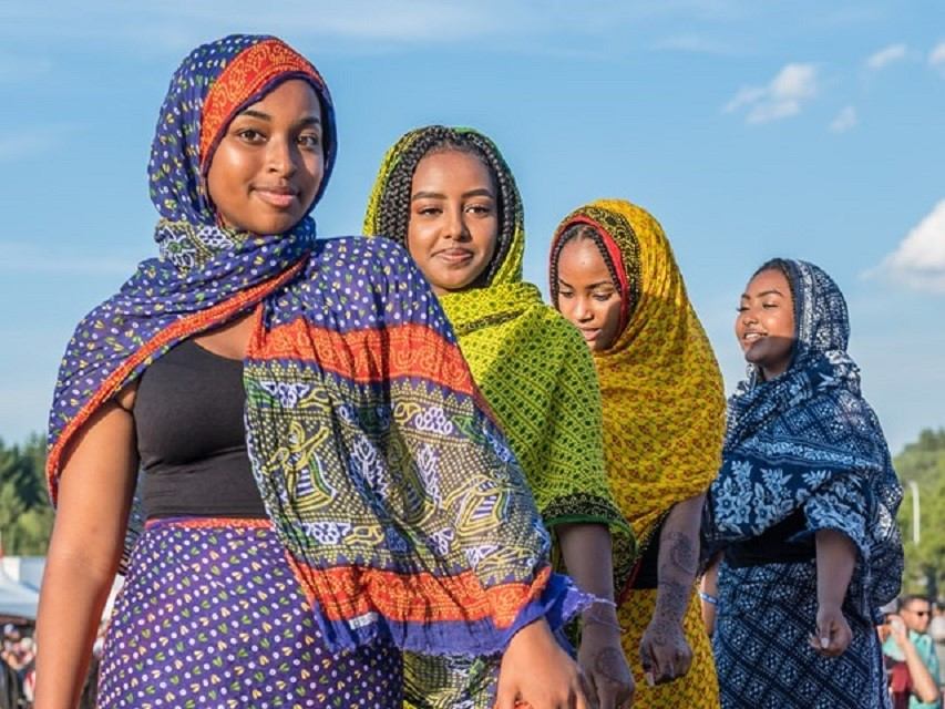 Costumed women in patterned headscarves and dresses posing outdoors at an Edmonton heritage festival.