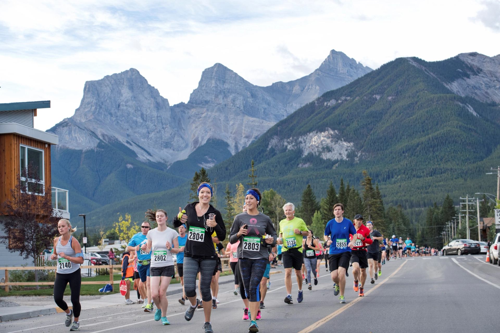 Runners in a road race pass buildings with Rocky Mountains in the background.