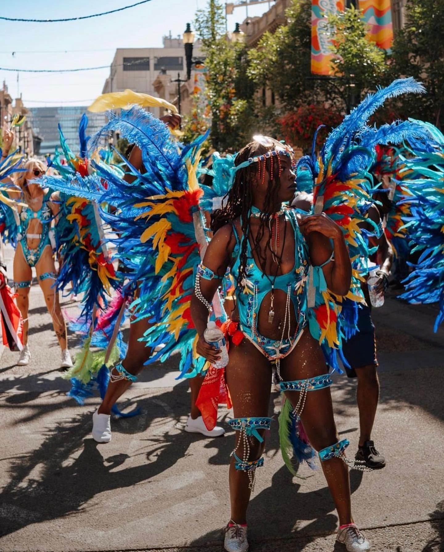 Parade participants in turquoise costumes with large blue feather wings on city street.